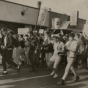 This is a picture depicting a multitude of students protesting on the street. They are holding up signs and protesting the change in the drinking age.